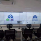Conference room with several ergonomic chairs around a long table; a wall of large video screens displays the Defensoría del Pueblo Colombia logo and microphones on the desk.